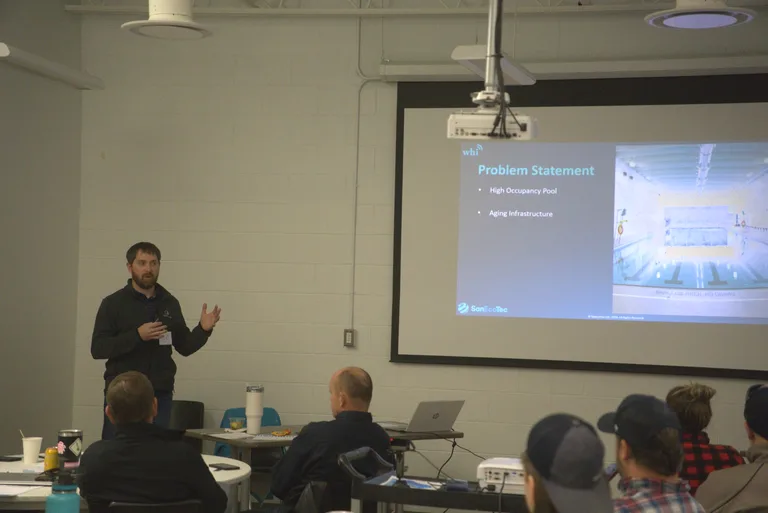 Presenter speaking beside a pool operations slide during the 2025 Better Pools Workshop